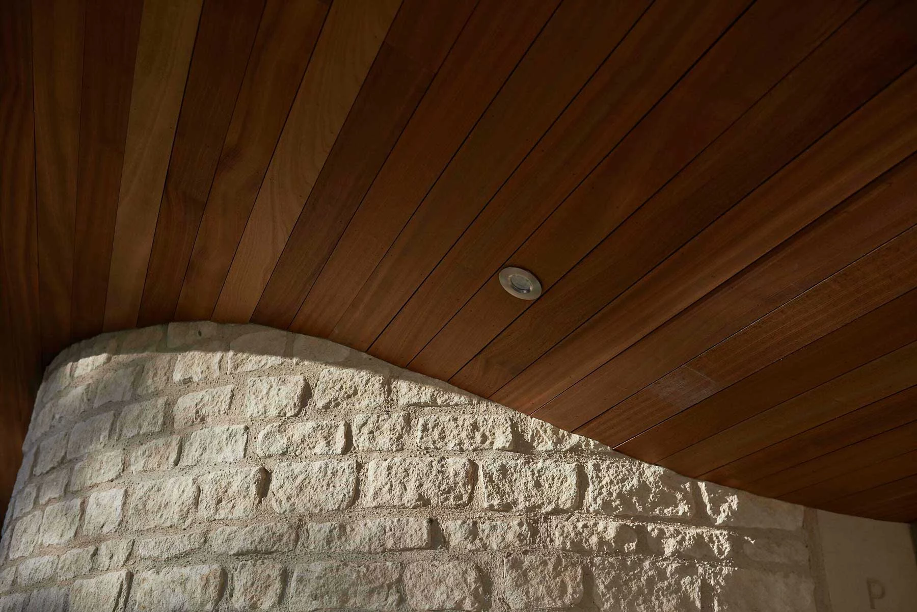 Detail shot of a bespoke curved Bath stone wall meeting a timber-clad soffit, showcasing precision masonry.